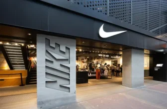 Nike retail store exterior with illuminated Swoosh logo and modern storefront entrance displaying sportswear inside
