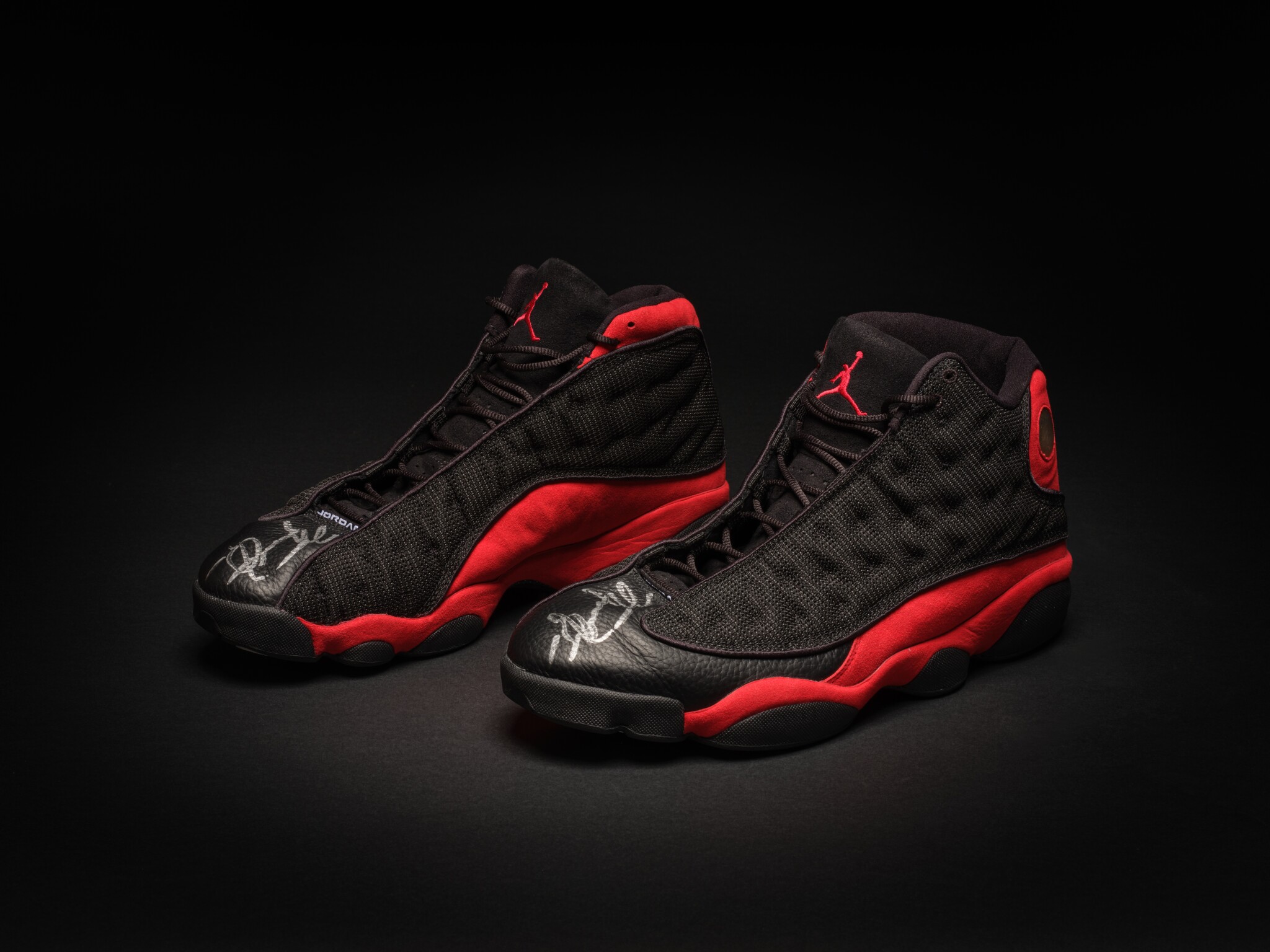 Black and red Air Jordan 13 basketball sneakers displayed on a dark background with signature Jumpman logo and sleek design